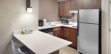 Guest room kitchen in Sonesta ES Suites Raleigh Durham Airport Morrisville, featuring fridge-freezer, hob, microwave, and table.