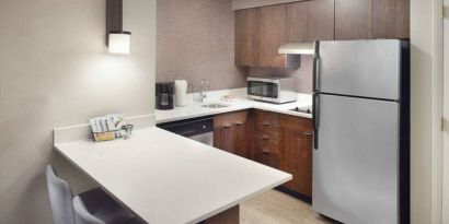 Guest room kitchen in Sonesta ES Suites Raleigh Durham Airport Morrisville, featuring fridge-freezer, hob, microwave, and table.