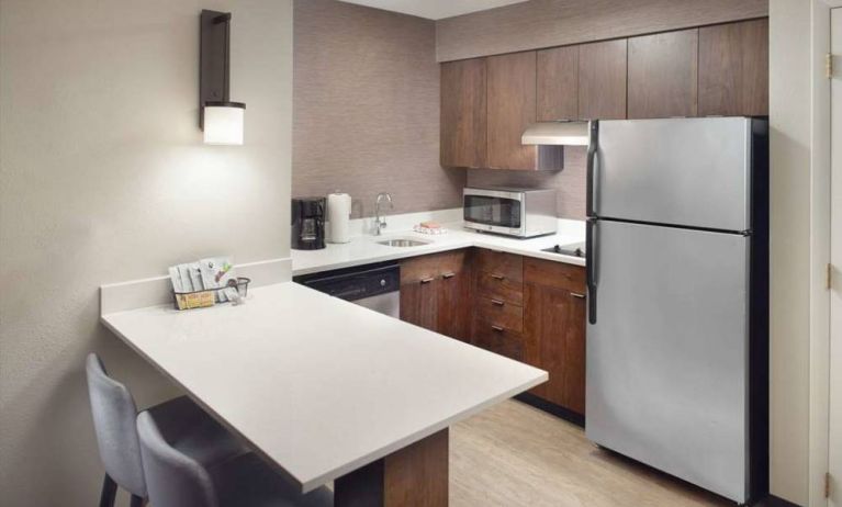 Guest room kitchen in Sonesta ES Suites Raleigh Durham Airport Morrisville, featuring fridge-freezer, hob, microwave, and table.