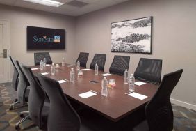 Hotel meeting room including long wooden table, 10 chairs, and a TV and art on the walls.