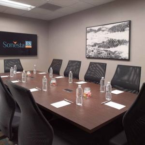 Hotel meeting room including long wooden table, 10 chairs, and a TV and art on the walls.