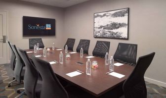 Hotel meeting room including long wooden table, 10 chairs, and a TV and art on the walls.