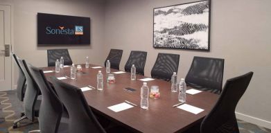 Hotel meeting room including long wooden table, 10 chairs, and a TV and art on the walls.