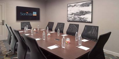 Hotel meeting room including long wooden table, 10 chairs, and a TV and art on the walls.