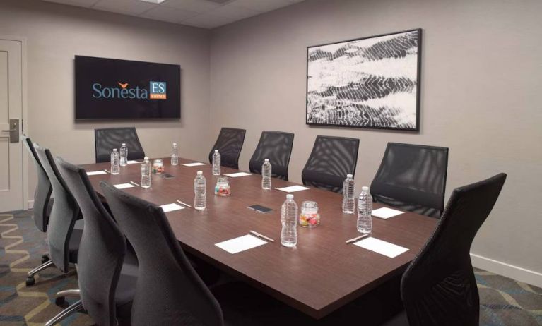 Hotel meeting room including long wooden table, 10 chairs, and a TV and art on the walls.