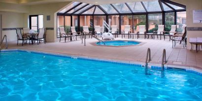 Indoor pool with nearby hot tub and lift, large windows and many chairs, at Sonesta Select Kansas City Airport Tiffany Springs.