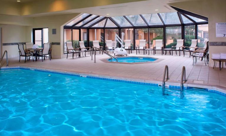 Indoor pool with nearby hot tub and lift, large windows and many chairs, at Sonesta Select Kansas City Airport Tiffany Springs.