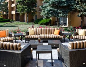 Patio area with sofa and armchair seating alongside coffee tables and pleasant greenery at Sonesta Select Kansas City Airport Tiffany Springs.