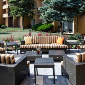 Patio area with sofa and armchair seating alongside coffee tables and pleasant greenery at Sonesta Select Kansas City Airport Tiffany Springs.