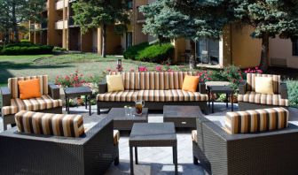 Patio area with sofa and armchair seating alongside coffee tables and pleasant greenery at Sonesta Select Kansas City Airport Tiffany Springs.