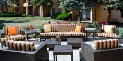 Patio area with sofa and armchair seating alongside coffee tables and pleasant greenery at Sonesta Select Kansas City Airport Tiffany Springs.