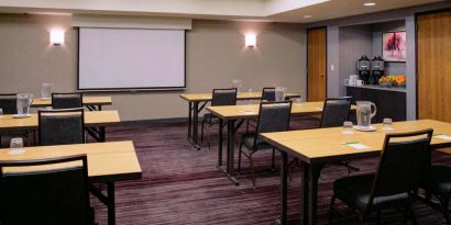 Hotel meeting room, with tables arranged in a classroom format facing a projector screen.