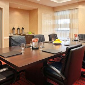 Hotel meeting room with long wooden table, large window, and eight leather chairs.