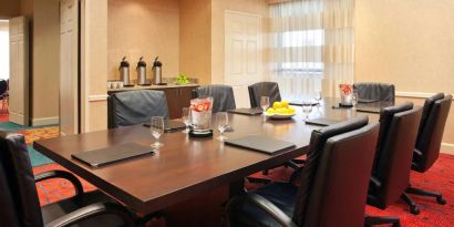 Hotel meeting room with long wooden table, large window, and eight leather chairs.