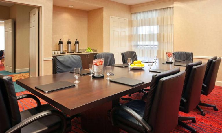 Hotel meeting room with long wooden table, large window, and eight leather chairs.