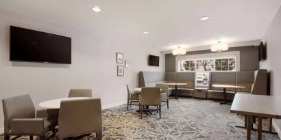 Lounge seating area, featuring tables and chairs, plus booth seating and a wall-mounted TV, at Sonesta ES Suites Reno.