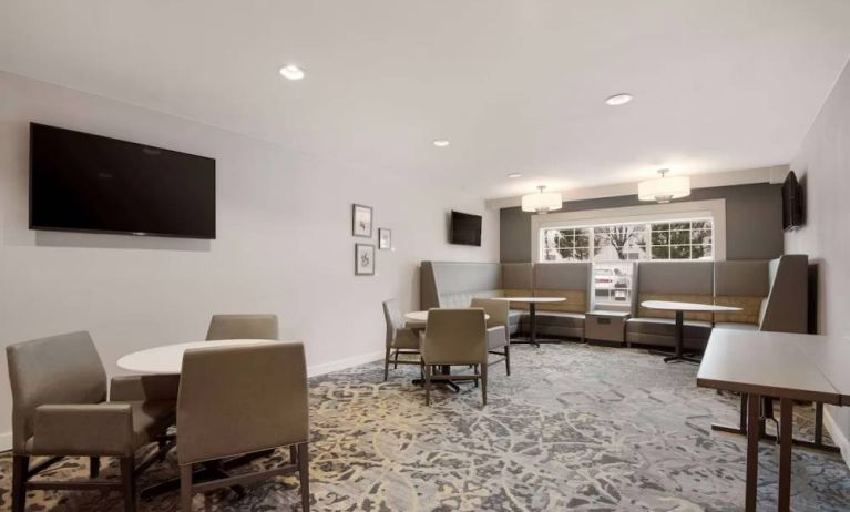 Lounge seating area, featuring tables and chairs, plus booth seating and a wall-mounted TV, at Sonesta ES Suites Reno.