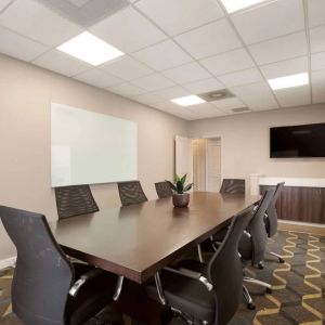 Hotel meeting room furnished with long wooden table, eight swivel chairs, a whiteboard, and a wall-mounted television.