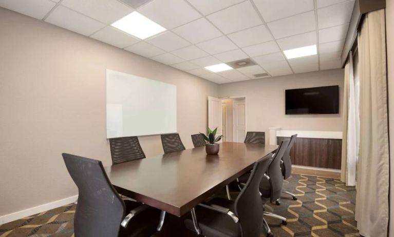 Hotel meeting room furnished with long wooden table, eight swivel chairs, a whiteboard, and a wall-mounted television.