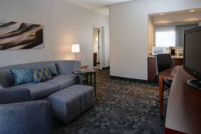 Guest room living area with sofa, chair, and TV at Sonesta Select Kansas City South Overland Park.