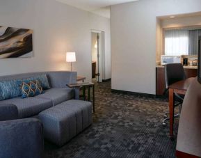 Guest room living area with sofa, chair, and TV at Sonesta Select Kansas City South Overland Park.