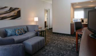 Guest room living area with sofa, chair, and TV at Sonesta Select Kansas City South Overland Park.