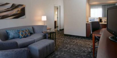 Guest room living area with sofa, chair, and TV at Sonesta Select Kansas City South Overland Park.