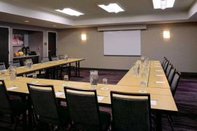 Hotel meeting room with a projector screen and tables arranged in a U-shape.