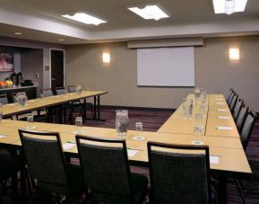 Hotel meeting room with a projector screen and tables arranged in a U-shape.