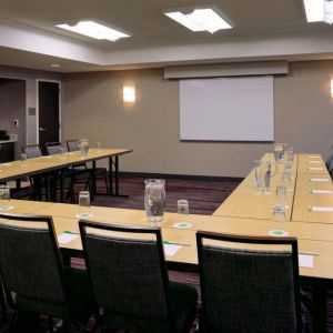 Hotel meeting room with a projector screen and tables arranged in a U-shape.