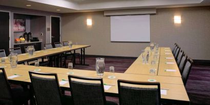 Hotel meeting room with a projector screen and tables arranged in a U-shape.