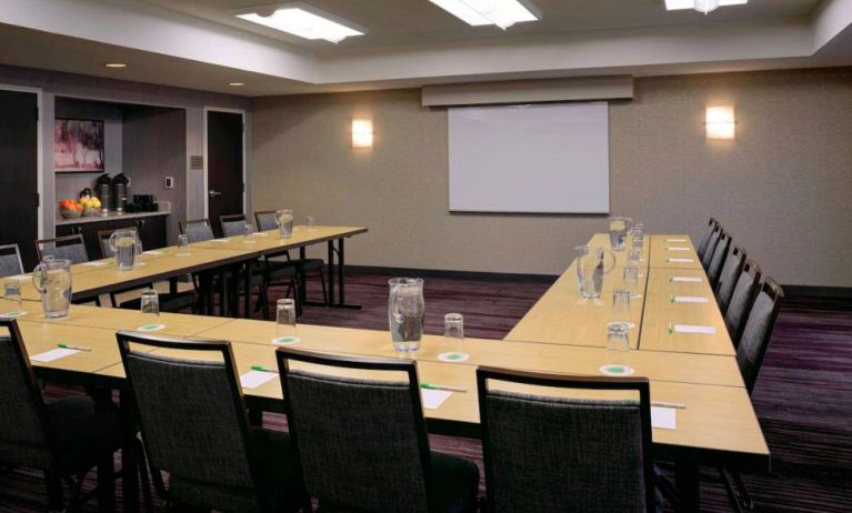 Hotel meeting room with a projector screen and tables arranged in a U-shape.