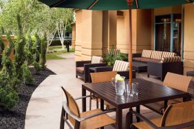 Patio area with shaded tables and chairs, plus armchair and sofa seating, near to pleasant greenery in Sonesta Select Pleasant Hill.