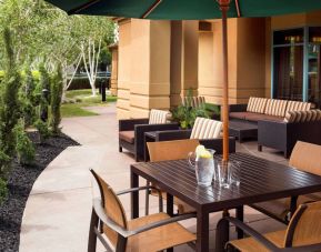 Patio area with shaded tables and chairs, plus armchair and sofa seating, near to pleasant greenery in Sonesta Select Pleasant Hill.