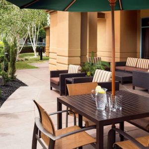 Patio area with shaded tables and chairs, plus armchair and sofa seating, near to pleasant greenery in Sonesta Select Pleasant Hill.