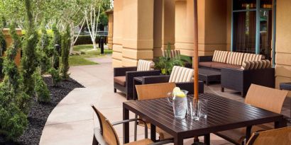 Patio area with shaded tables and chairs, plus armchair and sofa seating, near to pleasant greenery in Sonesta Select Pleasant Hill.