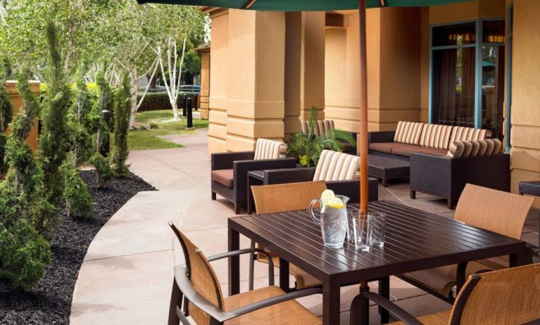 Patio area with shaded tables and chairs, plus armchair and sofa seating, near to pleasant greenery in Sonesta Select Pleasant Hill.