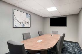 Hotel meeting room with wooden table, half a dozen chairs, and a wall-mounted television.