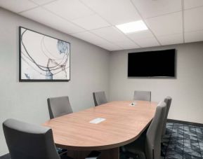 Hotel meeting room with wooden table, half a dozen chairs, and a wall-mounted television.