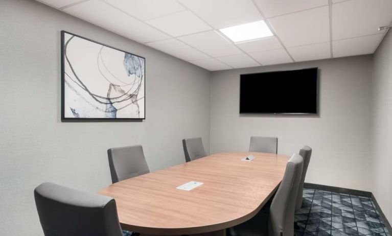 Hotel meeting room with wooden table, half a dozen chairs, and a wall-mounted television.