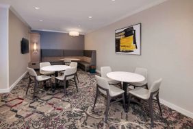 Lobby lounge in Sonesta ES Suites Atlanta Alpharetta North Point Mall with small tables and both art and a large TV on the wall.