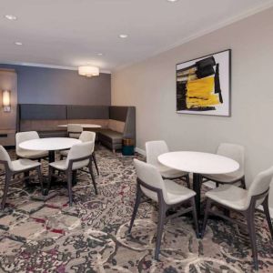 Lobby lounge in Sonesta ES Suites Atlanta Alpharetta North Point Mall with small tables and both art and a large TV on the wall.