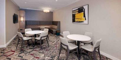 Lobby lounge in Sonesta ES Suites Atlanta Alpharetta North Point Mall with small tables and both art and a large TV on the wall.