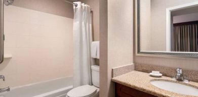 Sonesta ES Suites Tempe guest bathroom, fitted with shower-equipped bath, lavatory, mirror, and sink.