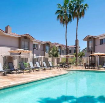 Outdoor pool at Sonesta ES Suites Tempe, featuring shaded tables and chairs, plus sun loungers, by the side.