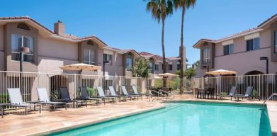 Outdoor pool at Sonesta ES Suites Tempe, featuring shaded tables and chairs, plus sun loungers, by the side.