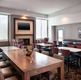 Breakfast area in Sonesta ES Suites Tempe, with mix of table sizes, sofas and chairs, large windows, and a wall-mounted television.