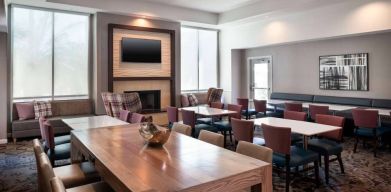 Breakfast area in Sonesta ES Suites Tempe, with mix of table sizes, sofas and chairs, large windows, and a wall-mounted television.