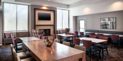 Breakfast area in Sonesta ES Suites Tempe, with mix of table sizes, sofas and chairs, large windows, and a wall-mounted television.