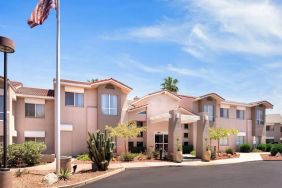 The hotel’s exterior has a fluttering USA flag flying from a flagpole and greenery including bushes, small trees, and a cactus.